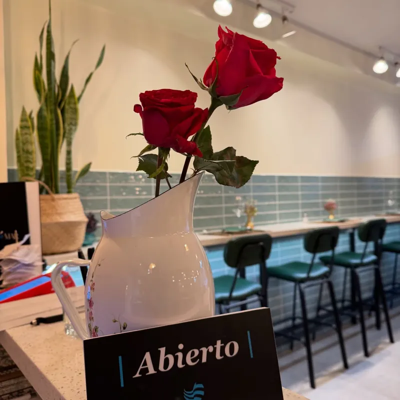 Rosas rojas en un jarro blanco junto a un cartel que dice Abierto